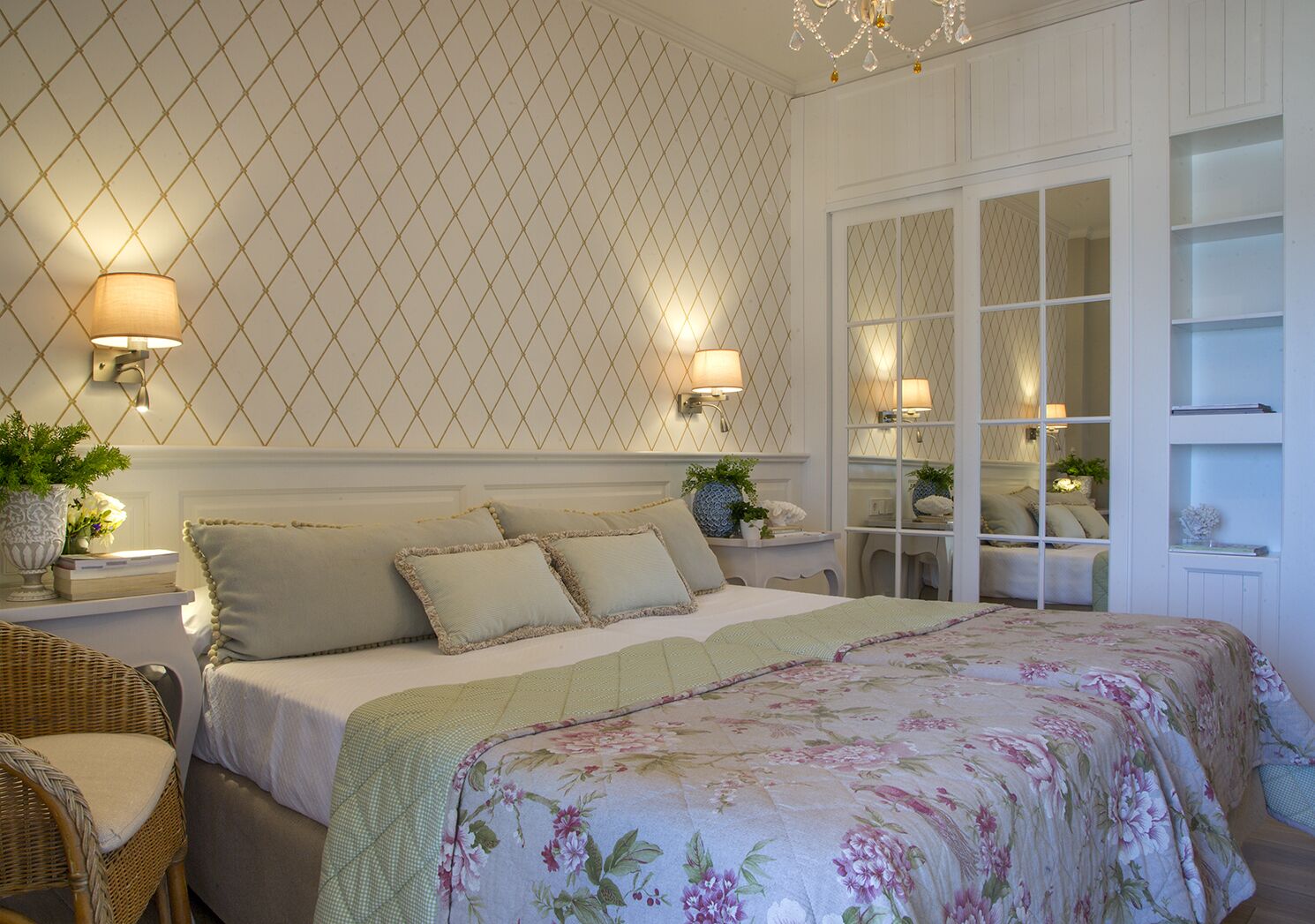 A bedroom with a large bed, two bedside lamps, a nightstand with a plant, and a mirrored closet with shelves.