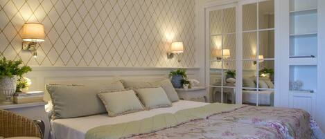 A bedroom with a large bed, two bedside lamps, a nightstand with a plant, and a mirrored closet with shelves.