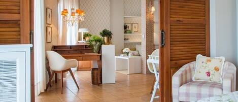 A bedroom with a bed, a chair, a desk, and a kitchenette area.