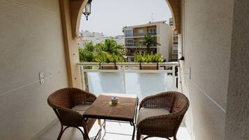 A balcony with wicker chairs and a table, overlooking a residential area with buildings and greenery.