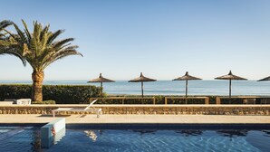 A pool area with a palm tree, lounge chairs, and umbrellas overlooking the sea. - Hotel Los Ángeles (Denia)