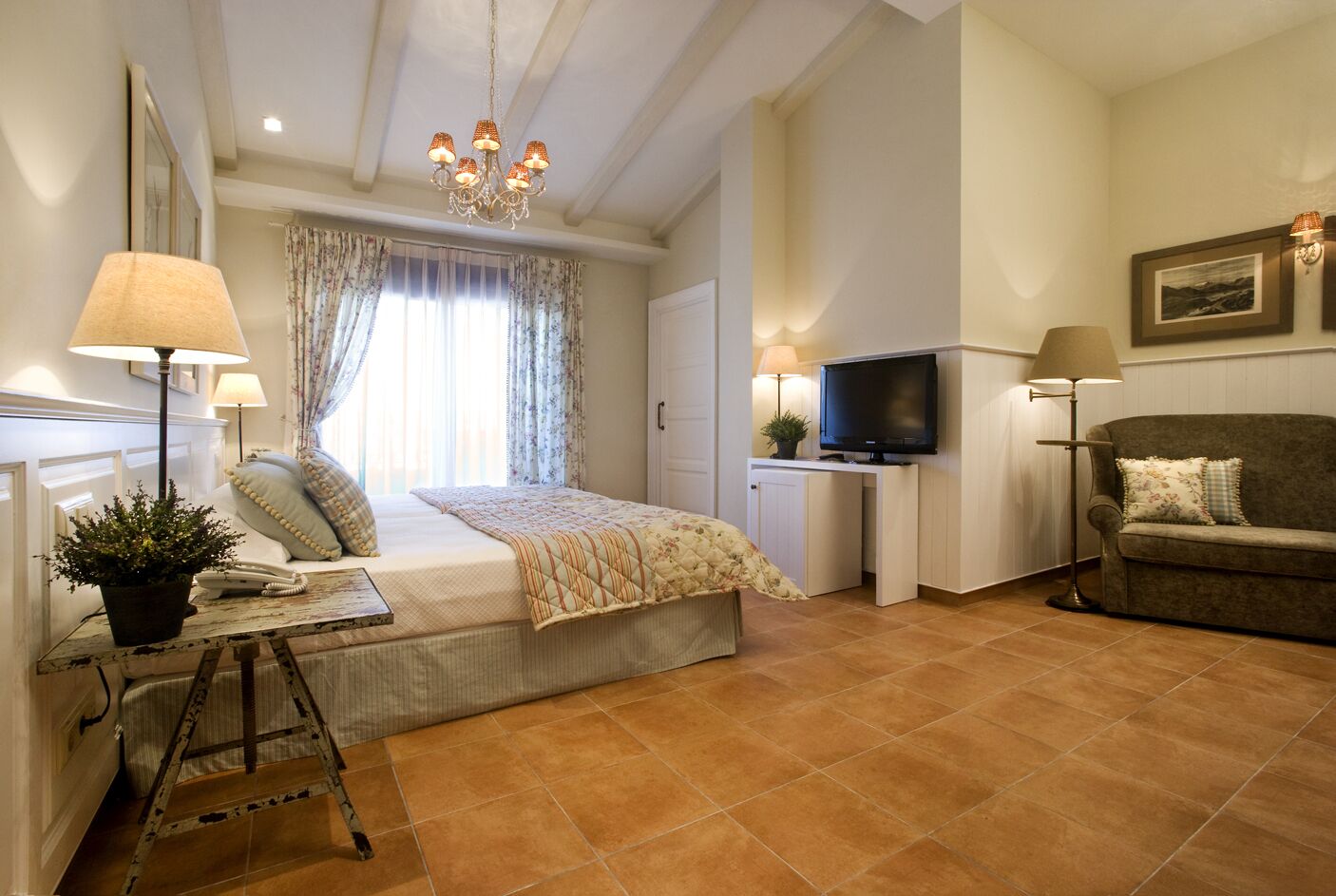 Un dormitorio con cama, lámparas de noche, televisión, sofá y escritorio con lámpara.