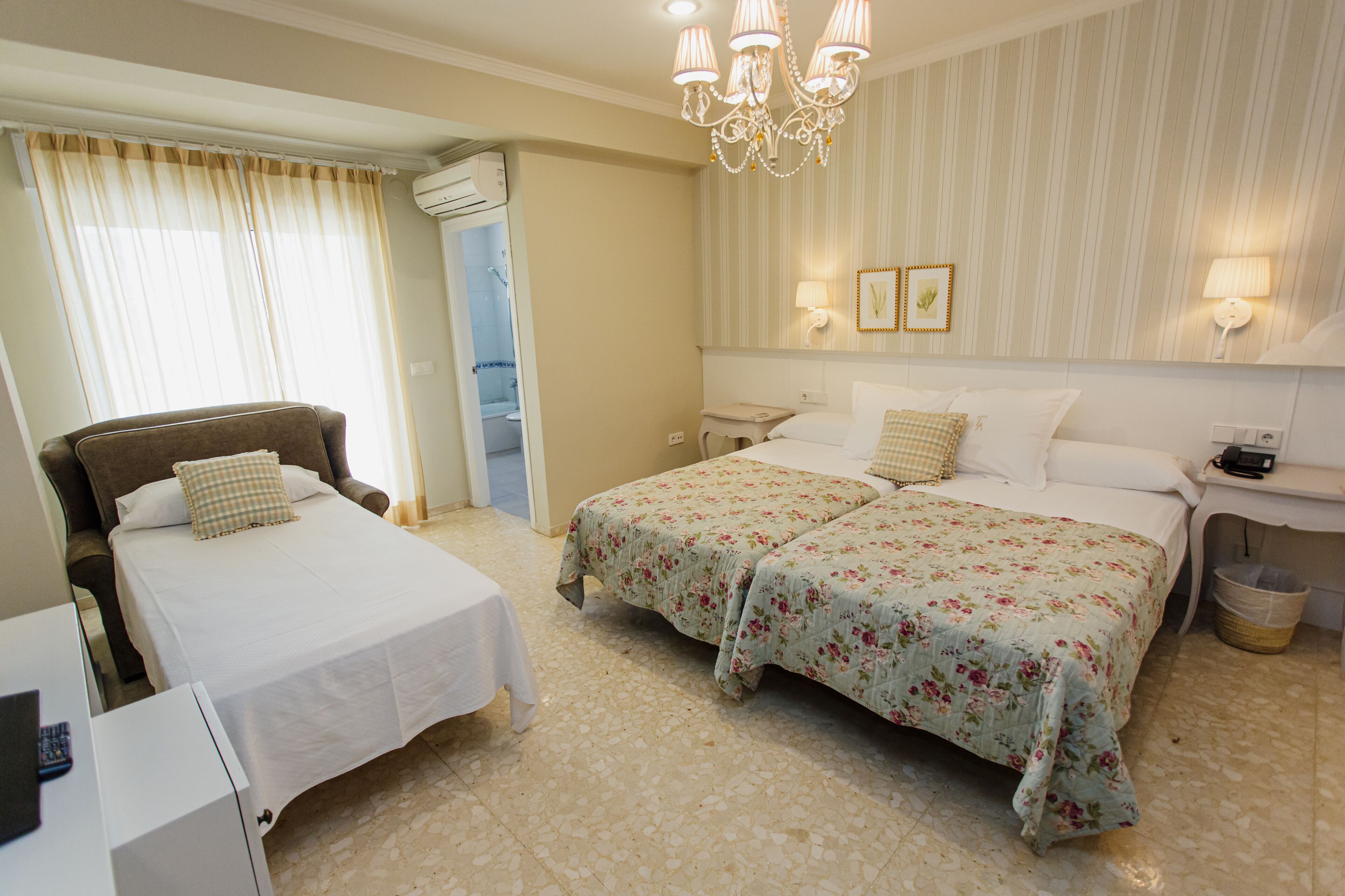A hotel room with two beds, a chair, a desk, and a bathroom.