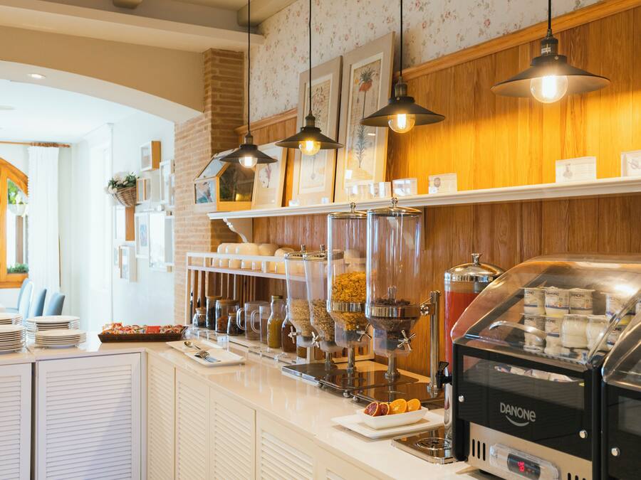 Zona de bufé con una máquina de café, dispensadores de alimentos y un mostrador con platos y cuencos.