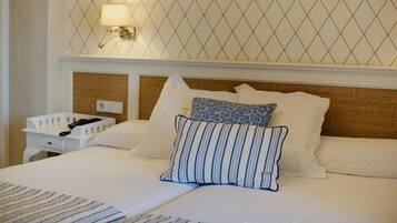A neatly made bed with white linens and blue-striped pillows, a bedside table with a lamp, and a wall with a geometric pattern.
