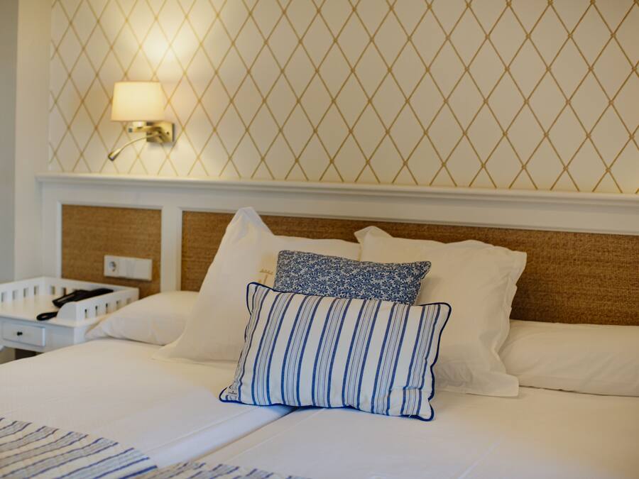 A neatly made bed with white linens and blue-striped pillows, a bedside table with a lamp, and a wall with a geometric pattern.