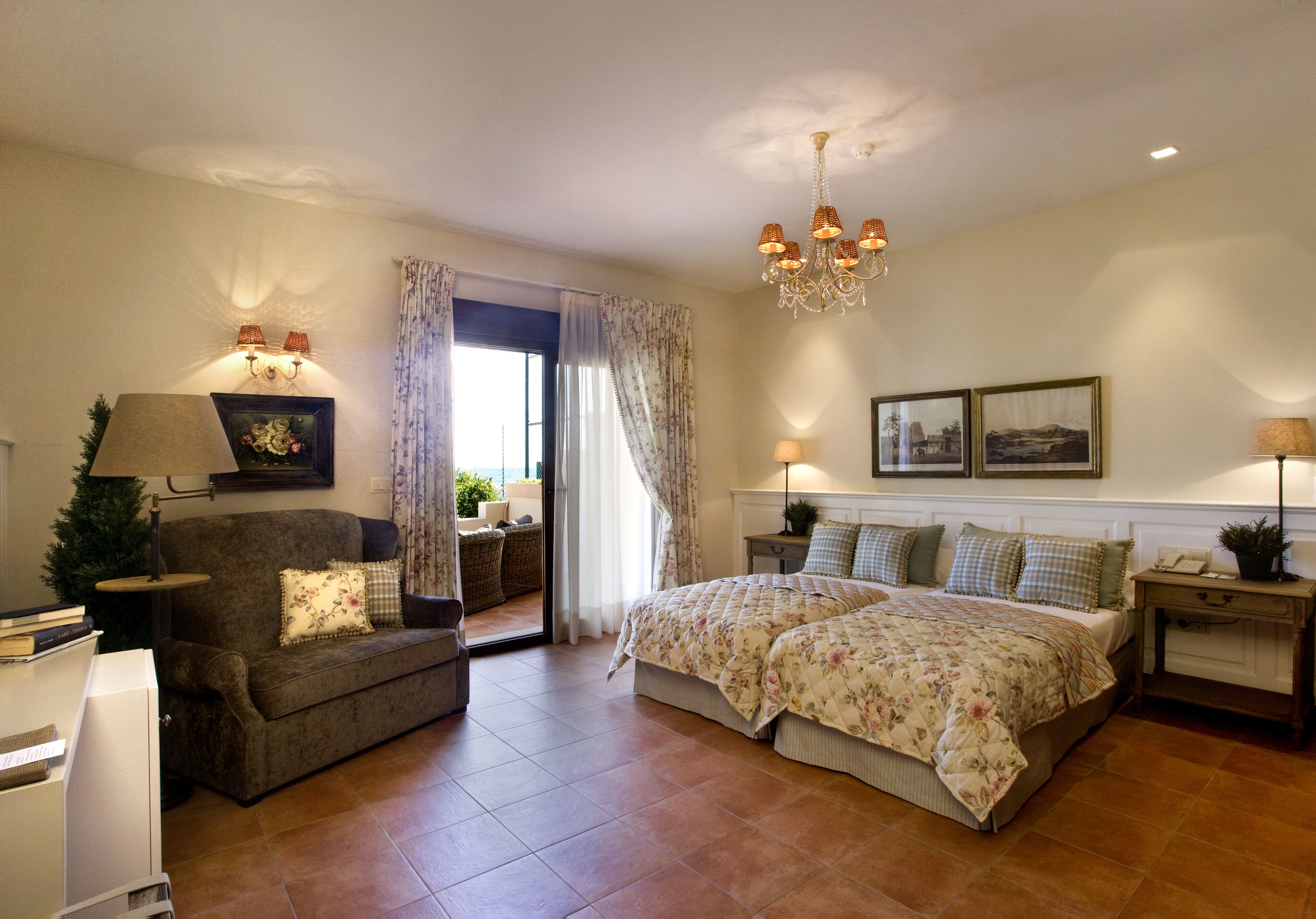 A spacious bedroom with a large bed, a sofa, a desk, and a chandelier.
