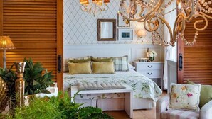 A bedroom with a bed, bedside tables, a chandelier, and a wall-mounted picture frame. - Hotel Los Ángeles (Denia)