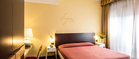 A hotel room with a bed, a nightstand, a lamp, a chair, and a wall with a name sign.