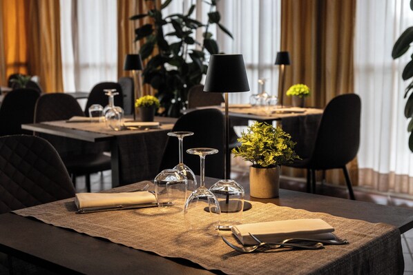 A dining area with tables set for a meal, clear glassware, and a potted plant.