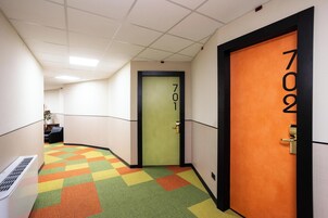 Un pasillo con una alfombra colorida, una puerta verde con la leyenda 701 y una puerta naranja con la leyenda 702.