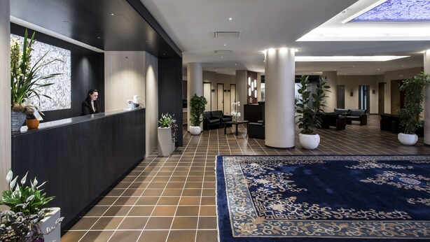 Un lobby moderno de hotel con una recepción, zona de estar y plantas en macetas.