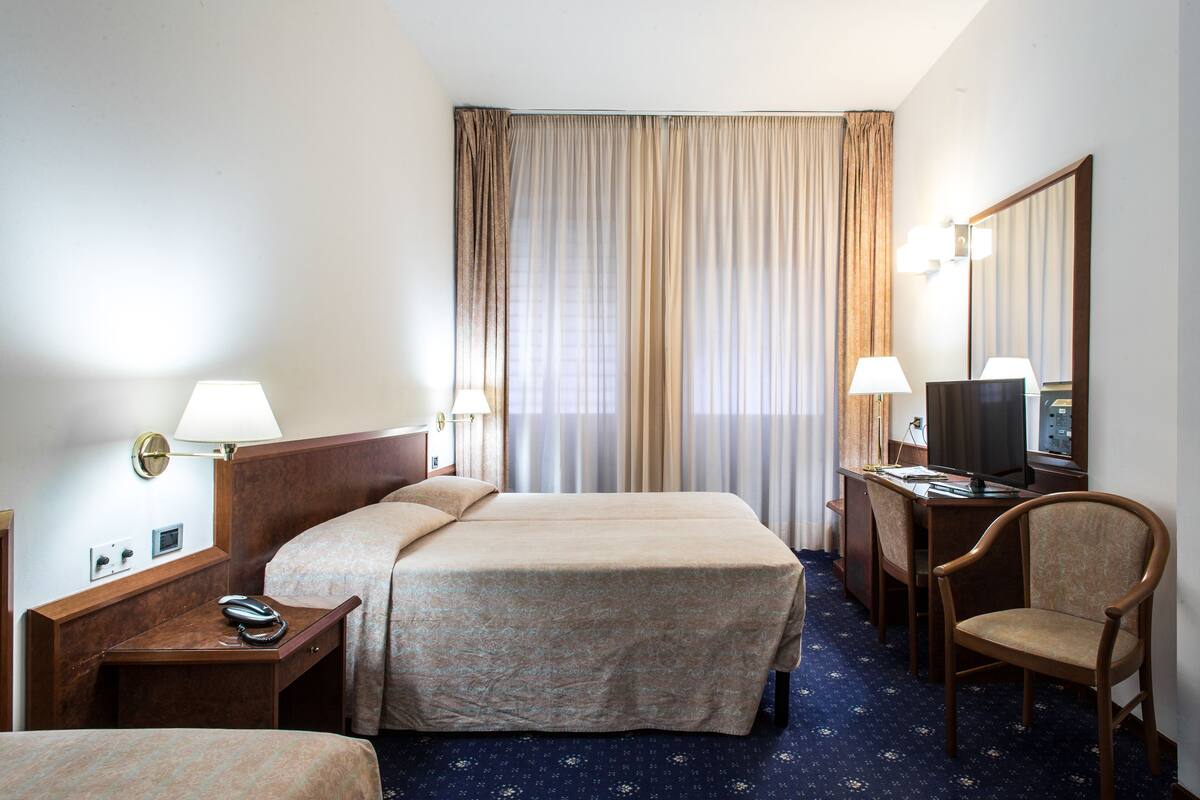 Habitación de hotel con dos camas, un escritorio con silla, televisor y espejo.