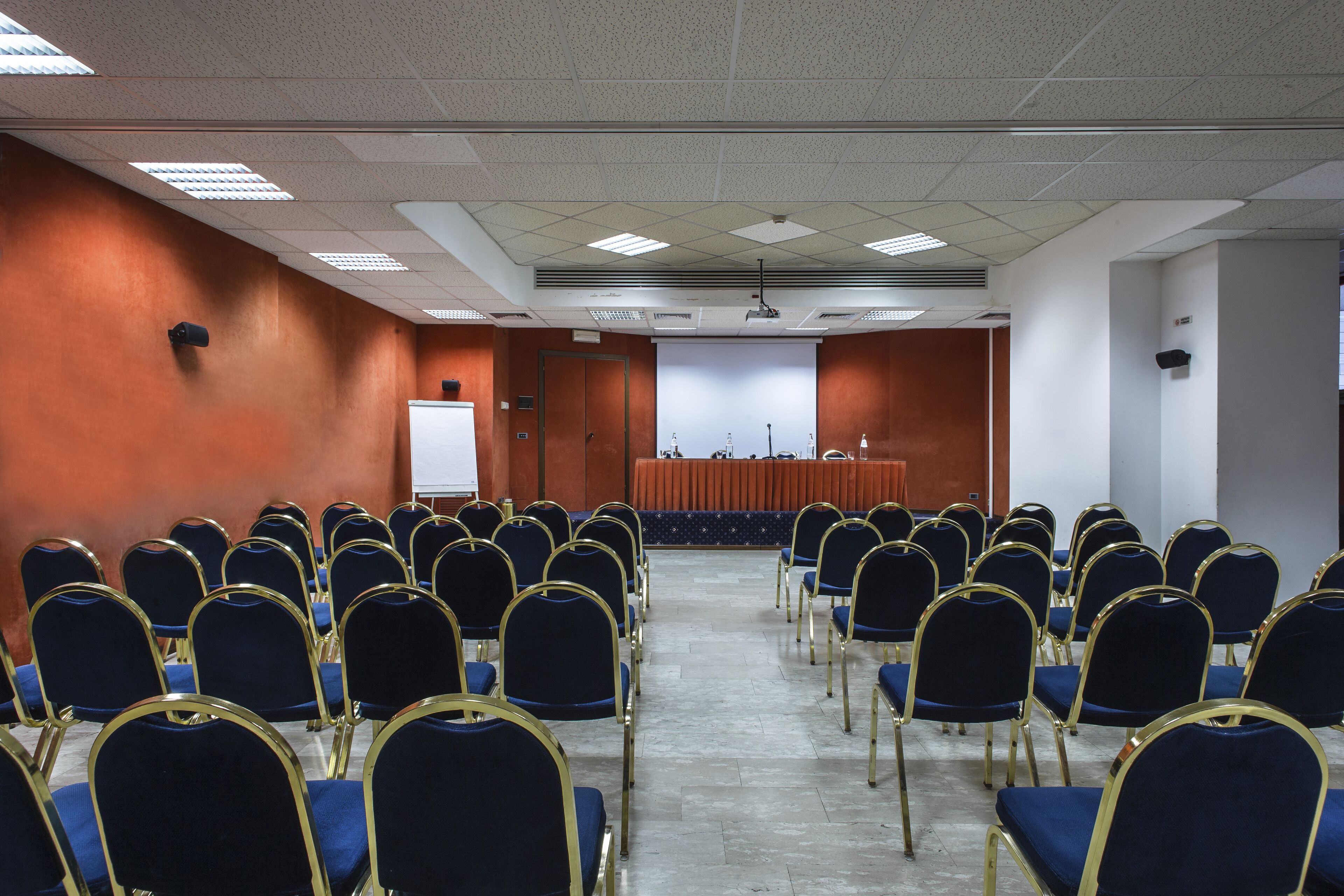 Un salón de conferencias con filas de sillas azules, un atril y una pizarra.