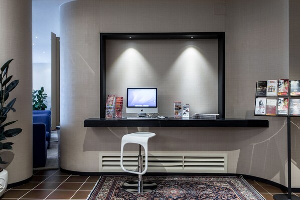 A modern reception area with a computer monitor, a white bar stool, and a display of magazines and brochures. - Hotel Mirage (Florence)