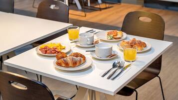 A breakfast table with croissants, sausages, scrambled eggs, and orange juice.