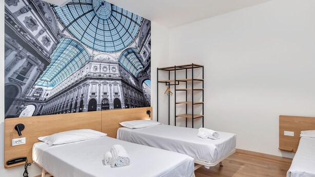 Une chambre d’hôtel avec deux lits, une armoire et une grande fresque murale représentant un bâtiment.