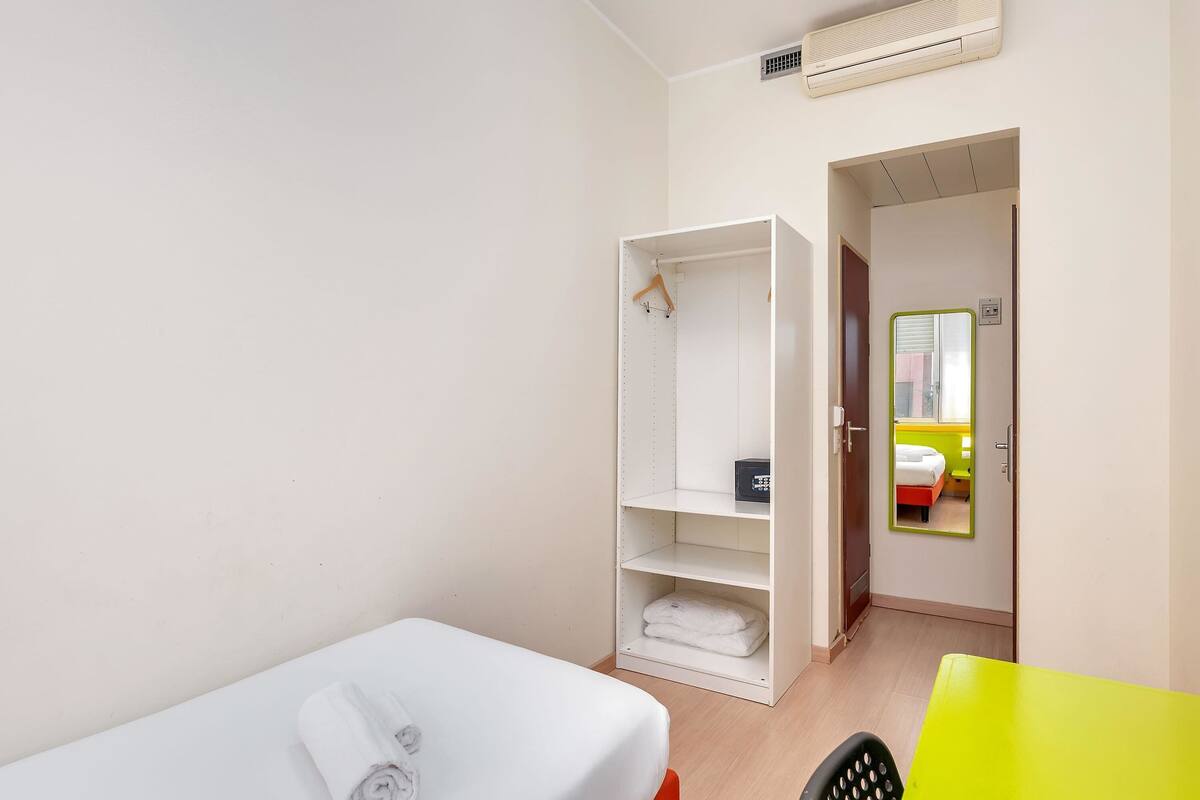 Hotellihuone, jossa on yksi sänky, vaatekaappi, pieni pöytä ja peili.