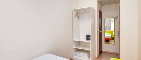 A hotel room with a single bed, a wardrobe, a small table, and a mirror.