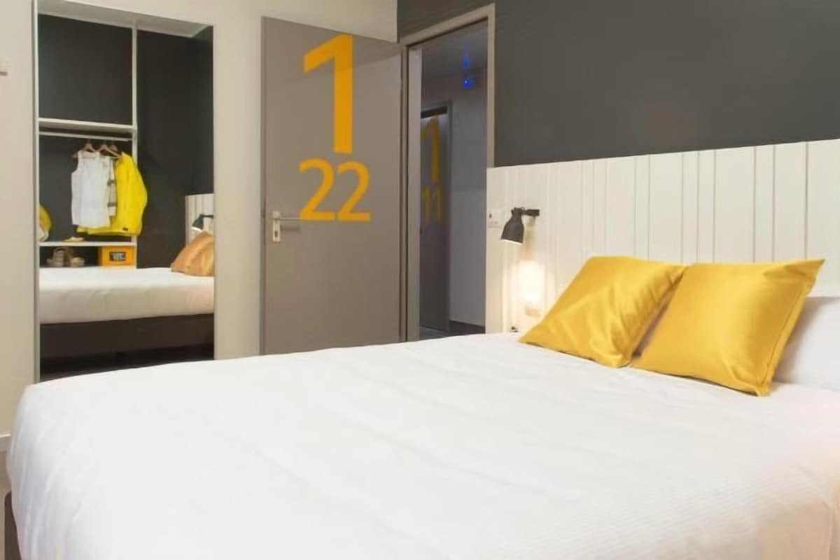 A hotel room with a bed, a wardrobe, and a door with numbers.