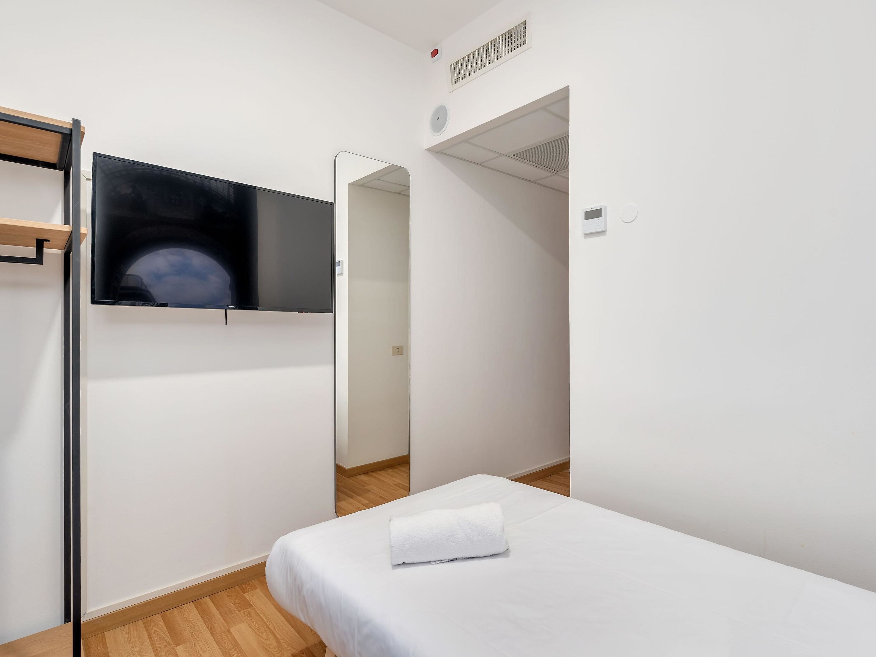 Habitación de hotel con cama, televisor montado en la pared, espejo y armario.