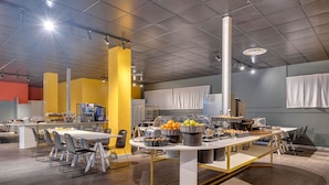 Un espace repas moderne, doté de plusieurs tables et chaises, d’un buffet proposant divers plats et d’une machine à café.