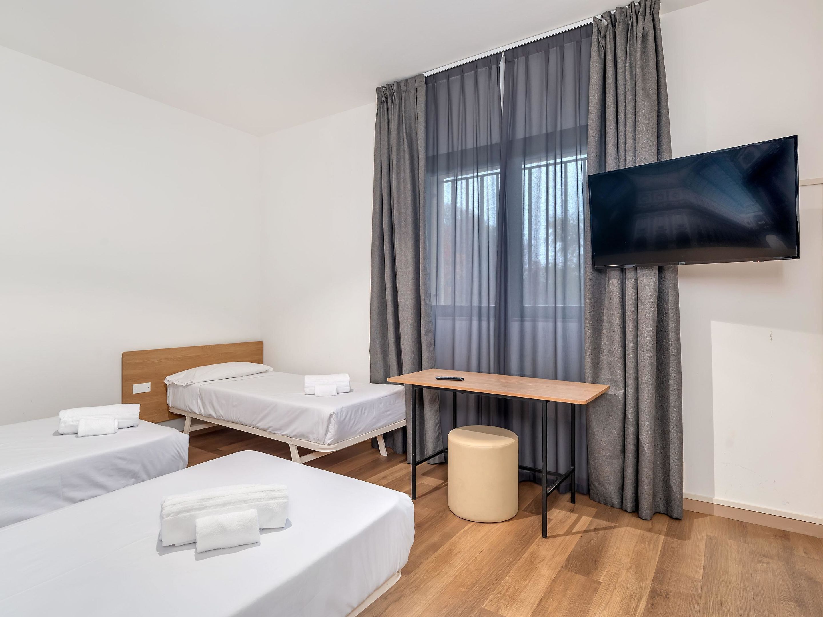 A hotel room with two single beds, a desk, a television, and a window with curtains.