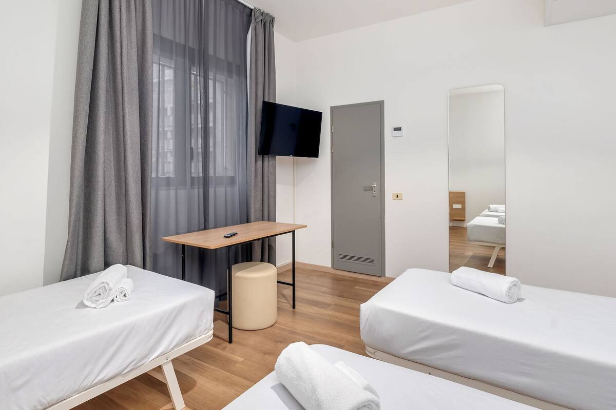 Hotellihuone, jossa on kaksi erillistä sänkyä, työpöytä, tuoli, televisio ja peili.