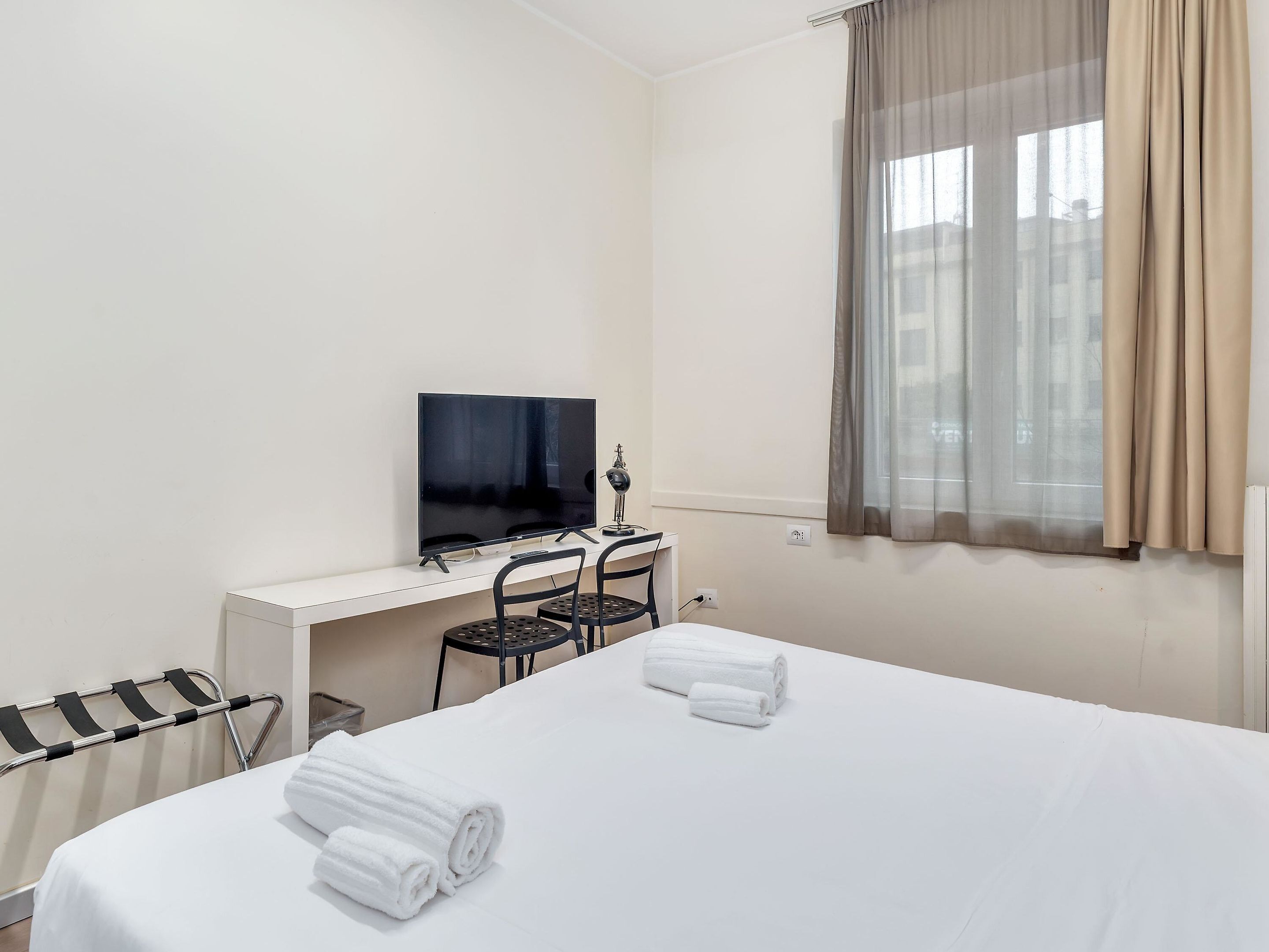 Une chambre d’hôtel avec un lit, un bureau avec une télévision, une chaise et une fenêtre avec des rideaux.