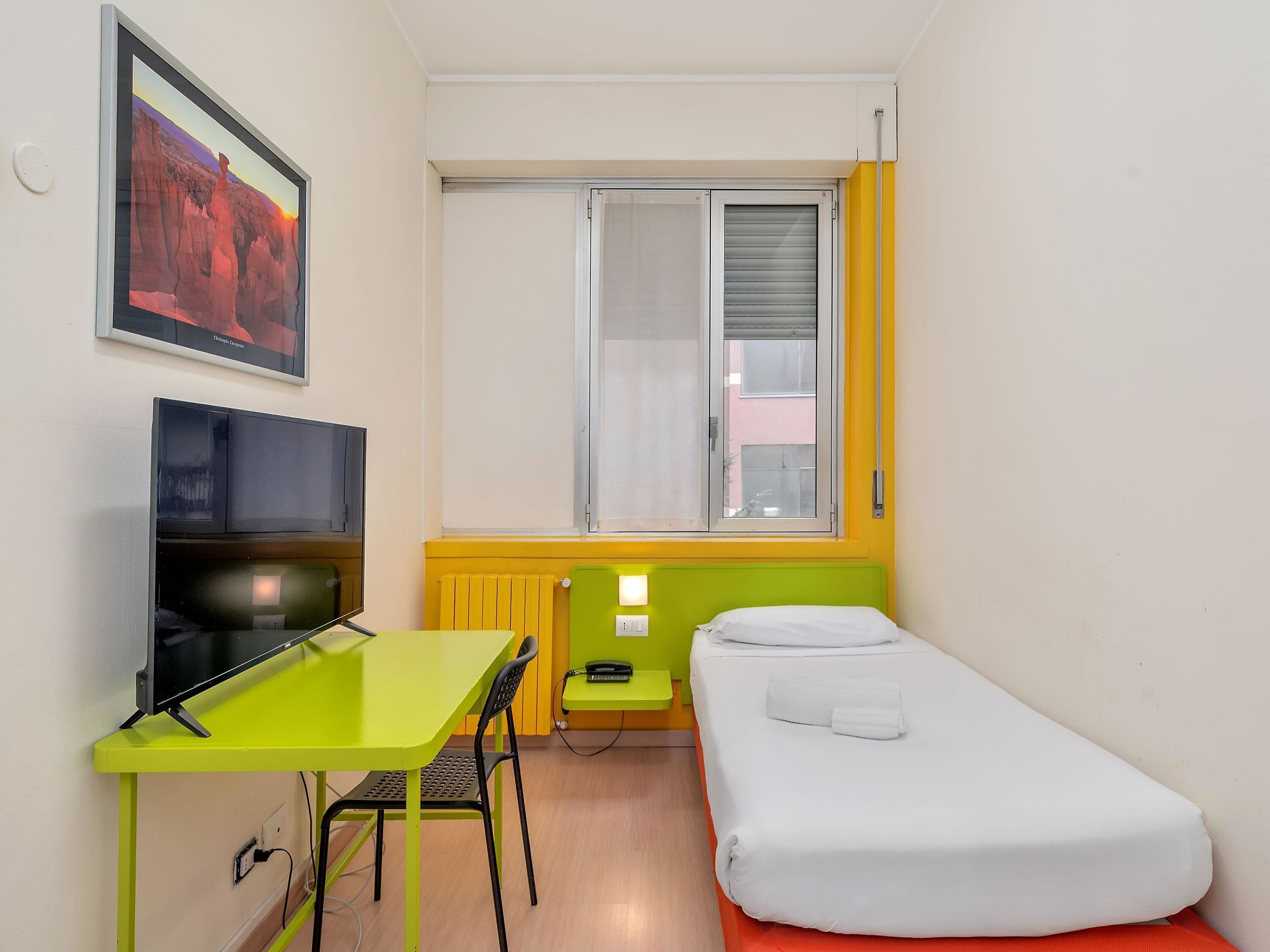 Een kleine, kleurrijke kamer met een enkel bed, een bureau en een televisie.