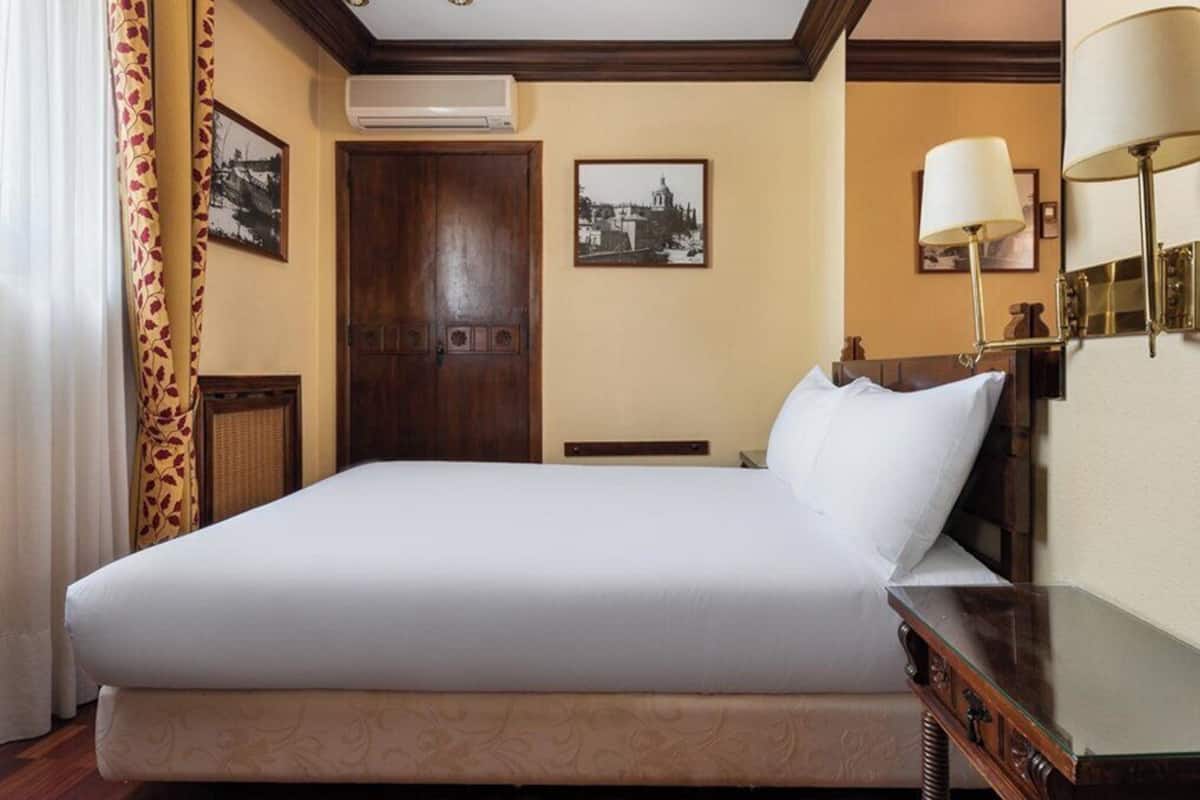 Habitación de hotel con una cama grande, una puerta de madera, un aire acondicionado montado en la pared y dos cuadros enmarcados.