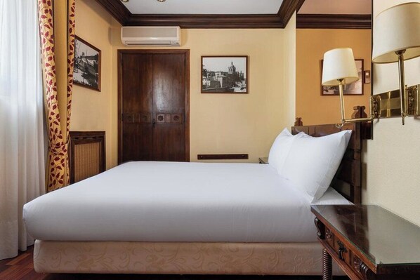 Habitación de hotel con una cama grande, una puerta de madera, un aire acondicionado montado en la pared y dos cuadros enmarcados.