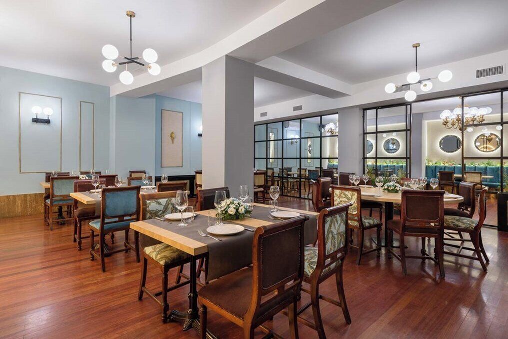 A spacious dining area with wooden tables and chairs, large windows with decorative mirrors, and modern lighting fixtures.