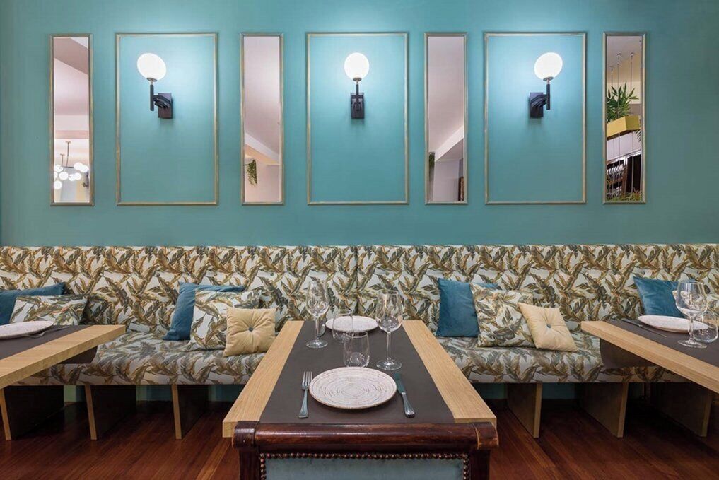 A dining area with a long table, two sofas, and wall-mounted mirrors.