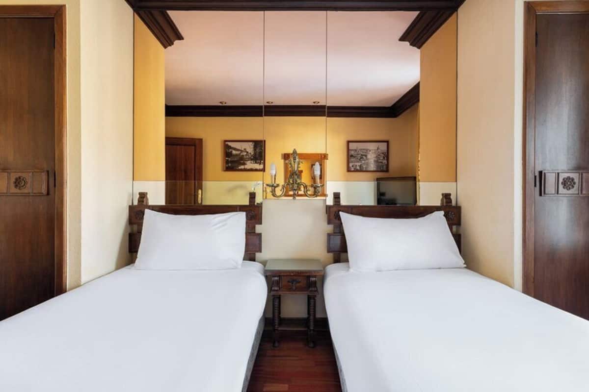 Una habitación de hotel con dos camas individuales, cabeceros de madera, una mesita y un televisor.