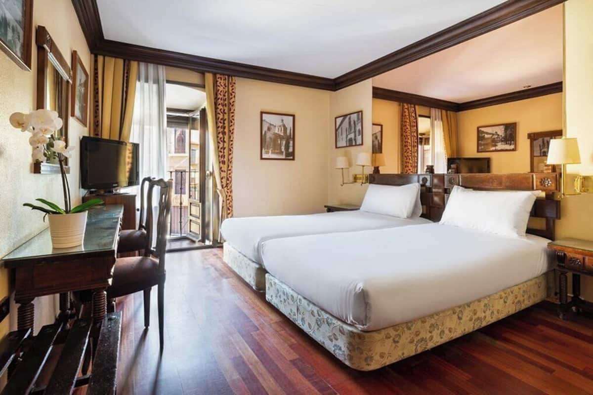 Habitación de hotel con dos camas, un escritorio con silla, un televisor y cuadros en las paredes.