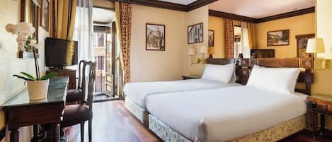 A hotel room with two beds, a desk with a chair, a television, and framed pictures on the walls.