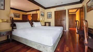 A large bed with a wooden headboard, a bedside table with a lamp, and a chair in a hotel room with wooden flooring and a wooden door.