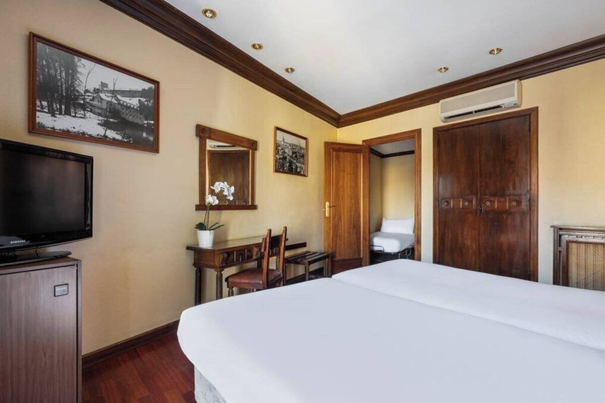 Una habitación de hotel con cama, escritorio, silla, televisor y armario.