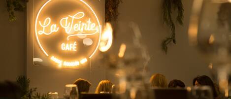 A café interior with a neon sign reading "La Teinte CAFÉ CONDE ROORIS".