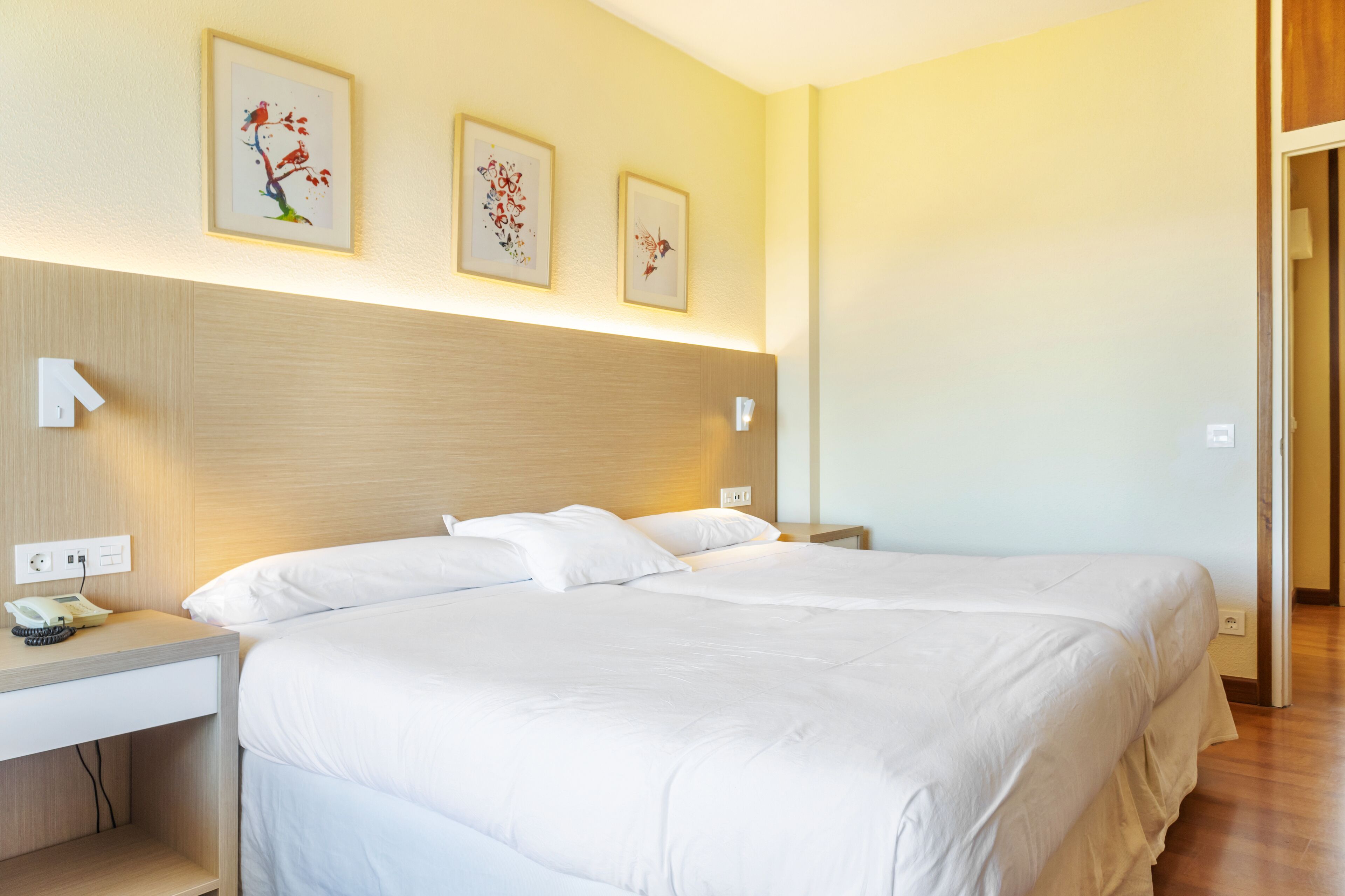 Habitación de hotel con dos camas, una mesita de noche con teléfono y una obra de arte en la pared.