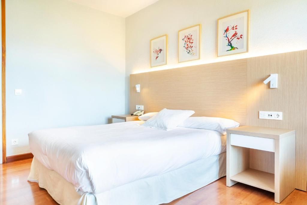 A hotel room with a bed, bedside tables, and wall-mounted artwork.