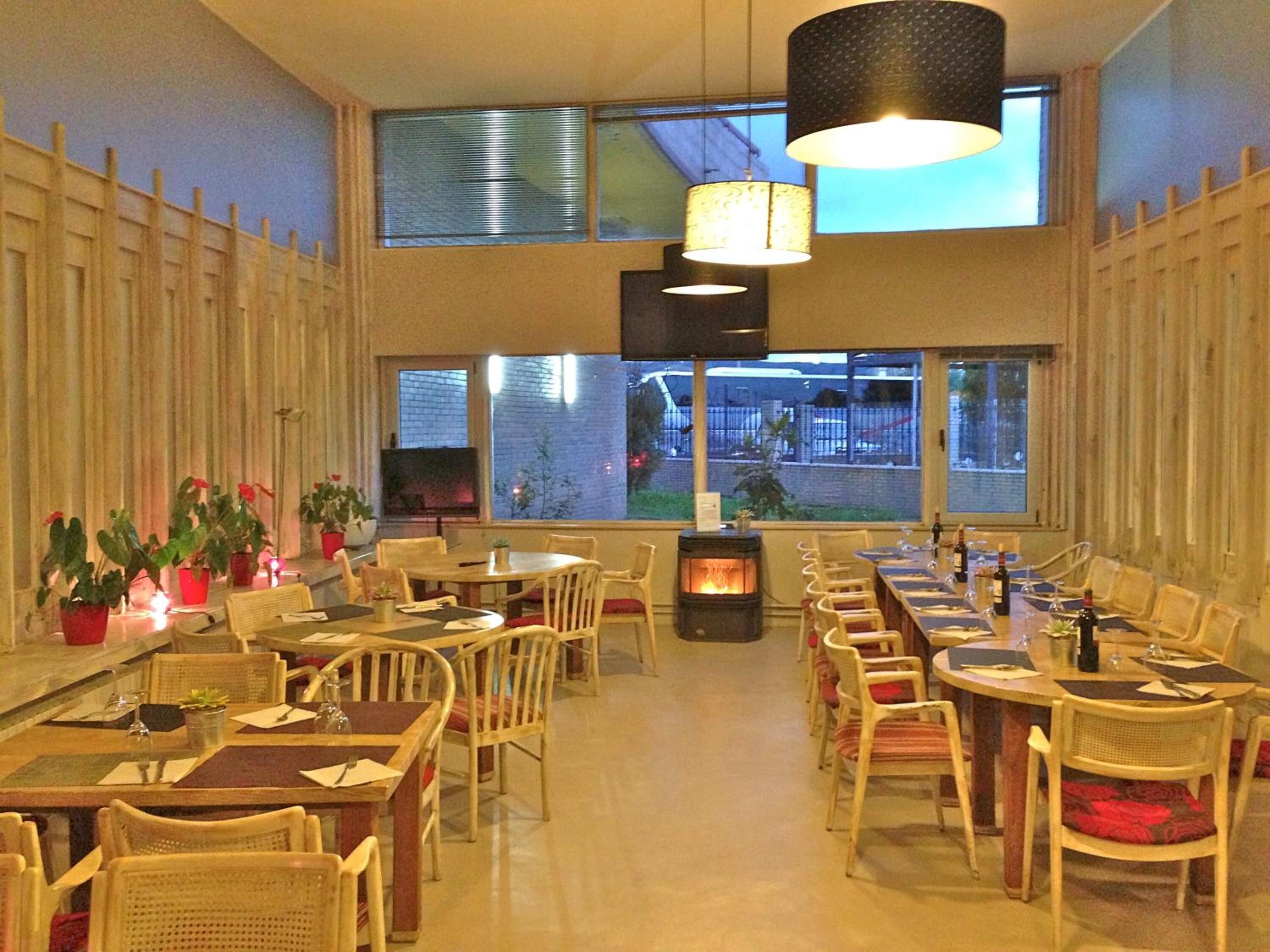Ein Restaurant mit mehreren Tischen und Stühlen, einem Kamin und großen Fenstern mit Blick ins Freie.