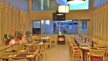 A restaurant with multiple tables and chairs, a fireplace, and large windows offering views of the outside.