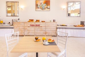 A breakfast setup with a wooden table, white chairs, and a buffet counter labeled 'CASA VEJO' with various food items. - Hotel Vejo (Reinosa)