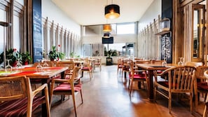 Un restaurante espacioso con mesas y sillas de madera, ventanas amplias y lámparas colgantes.