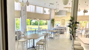 A spacious indoor dining area with multiple tables and chairs, large windows with curtains, and hanging spherical light fixtures. - Hotel Vejo (Reinosa)