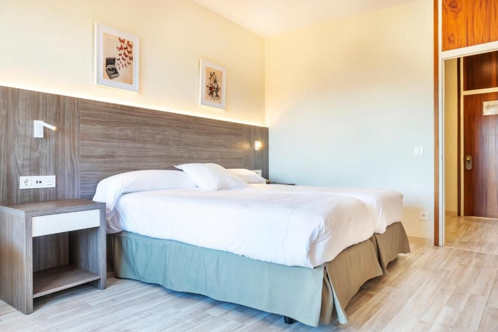 A bedroom with a bed, bedside tables, and wall-mounted light fixtures.