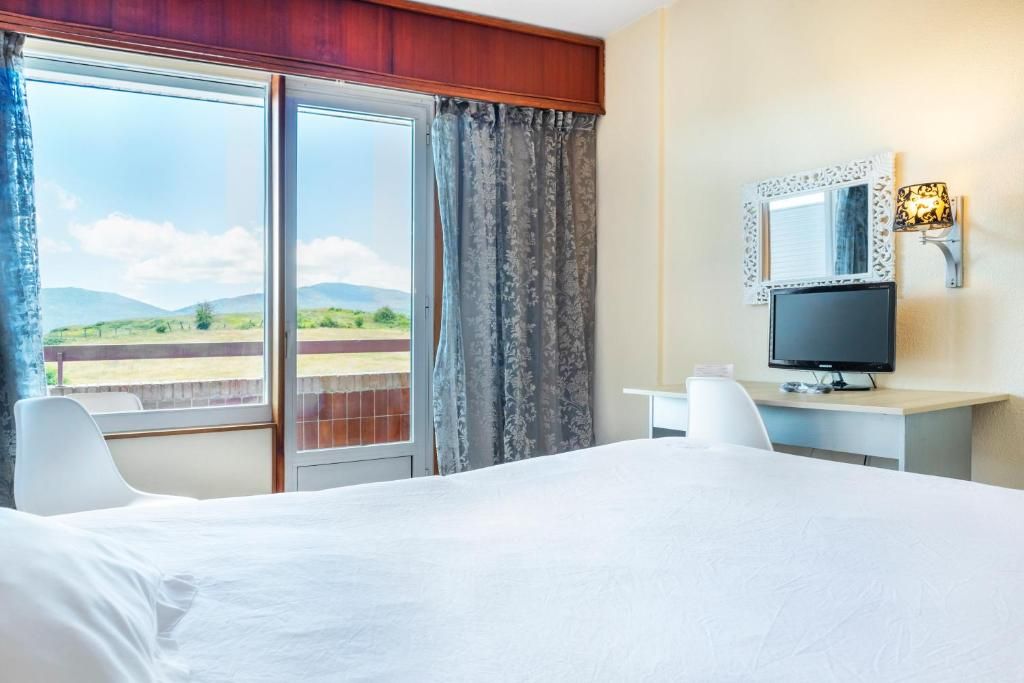 A hotel room with a bed, a desk, a television, and a window with curtains.