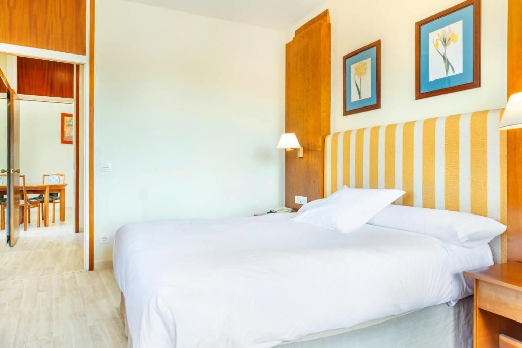 Una habitación de hotel con una cama, una mesita de noche, una lámpara y un cabecero de madera.